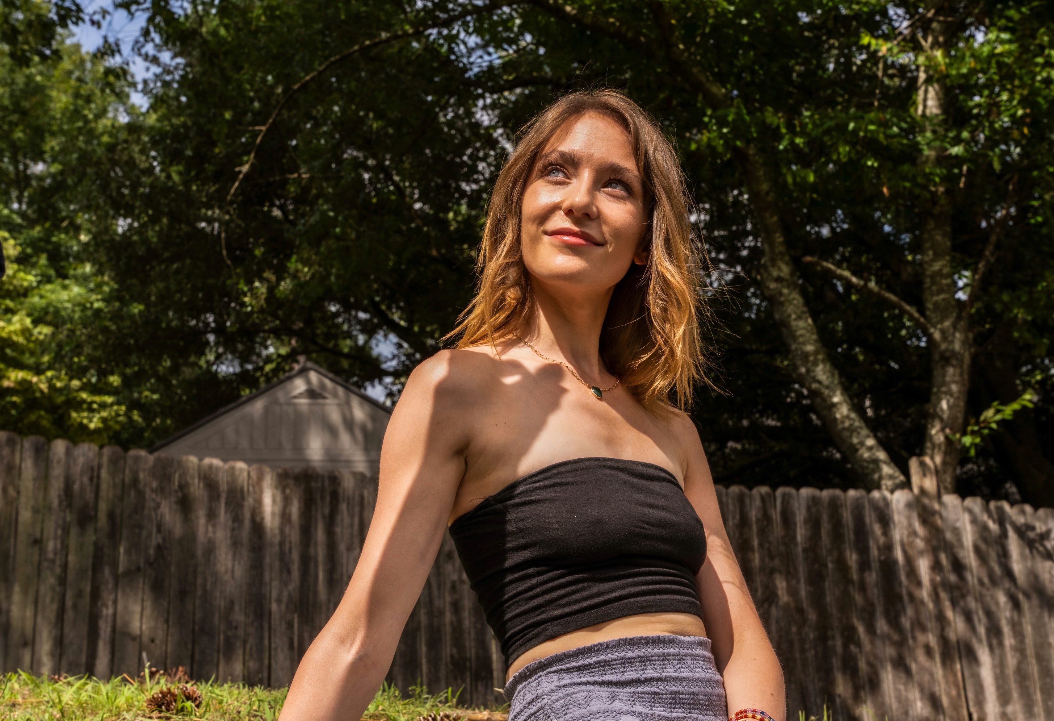 Becca outdoors in warm golden sunlight against a rustic fence