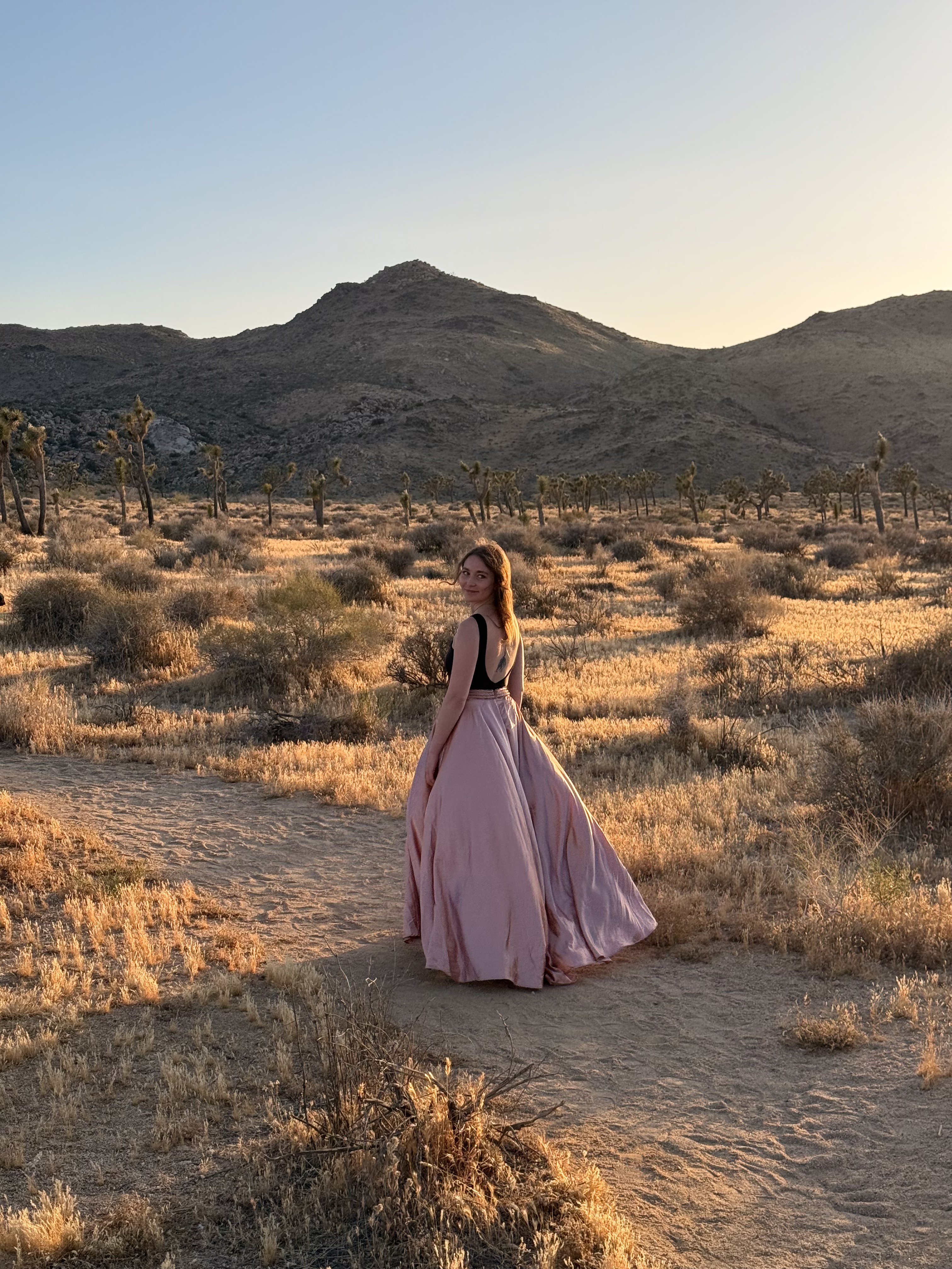 Becca in a flowing pink gown walking a desert path at dusk among Joshua trees